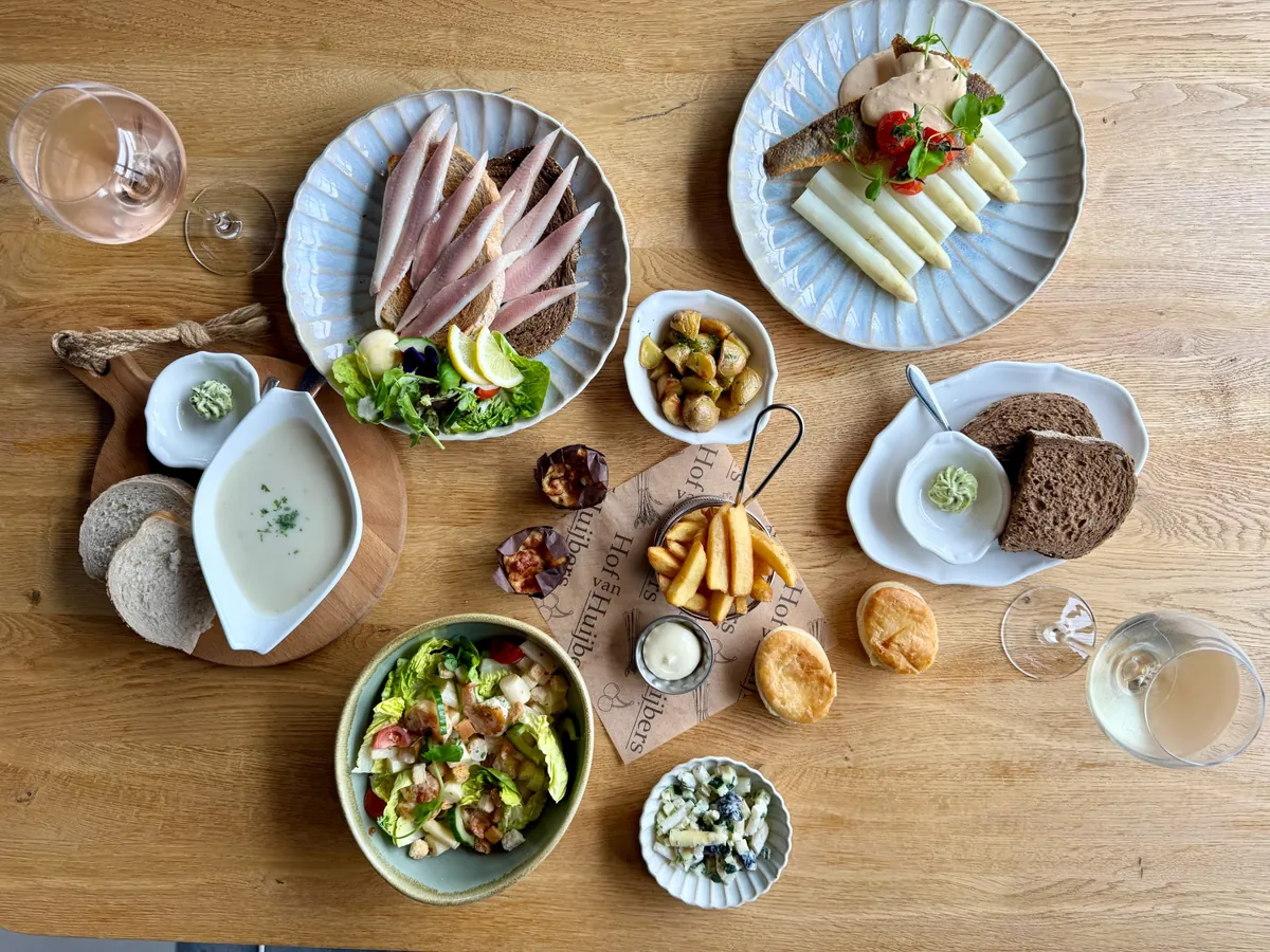 Gedekte tafel met lunchgerechten: asperges met vis, gerookte paling, aspergesoep, salade, friet en kroketjes